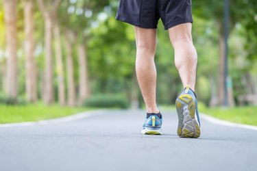 young adult caucasian male in sneakers running on a paved park trail