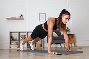 Person in a black sports bra and bike shorts performing a plank in their living room
