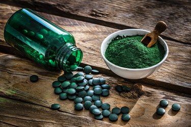 Spirulina powder and pills, a food high in GLA, scattered on rustic table