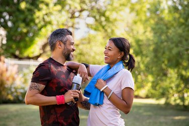 a couple smiling at each other taking a break after a jog in a park