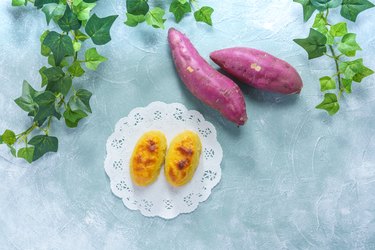 Two raw and one roasted japanese sweet potato over blue background.