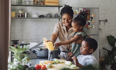 Mother, Daughter and Son Preparing Spaghetti and Vegetables for Lunch over a Cutting Board