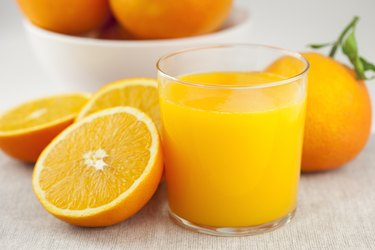 A glass of orange juice next to some orange slices, as an example of citrus fruits that cause diarrhea