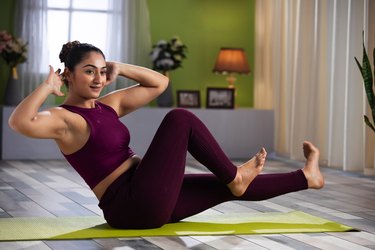 young Middle Eastern woman in a purple athletic outfit doing bodyweight exercises on a green yoga mat at home