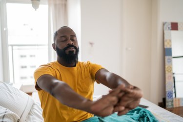 Person waking up and stretching in bed at home to ease morning joint pain.