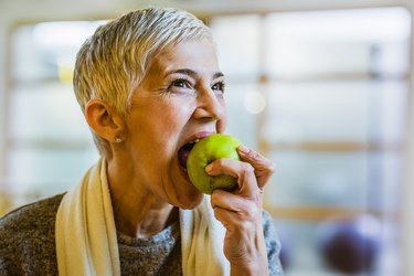 Mature athletic woman eating an apple after exercising in health club.