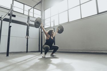 女人蹲在她的车库与杠铃执行开销。