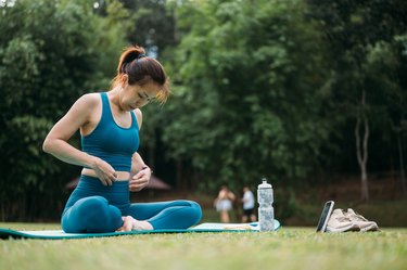 a person wearing an athletic clothing set sitting outside on the grass and doing pelvic floor breathing exercises