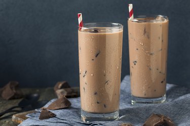 two glasses of chocolate milk with ice on a dark blue napkin