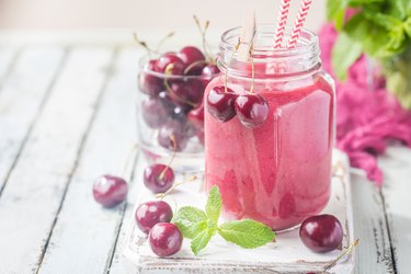 Healthy cherry drink on white wooden table with cherries