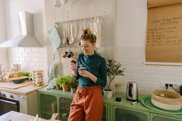 a woman eating a cup of yogurt in her kitchen, to help reduce inflammation