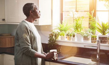 早晨，一位若有所思的老年妇女站在厨房里喝水