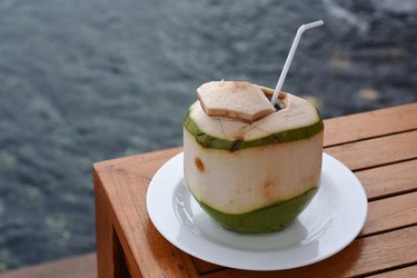 Fresh coconut water drink with white plate, on the corner of lattice table, beside the pool