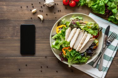 Healthy chicken salad next to smartphone on wood table background