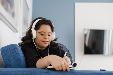 Person with down syndrome writing in book and listening to music at home.