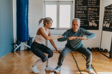 older man doing a squat with the help of a personal trainer