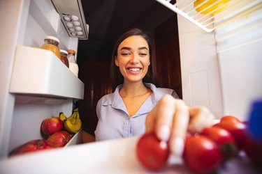 Young woman taking fresh healthy vegetables from fridge