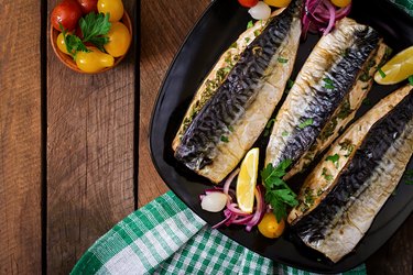 CoQ10-rich baked mackerel with herbs and garnished with lemon on a black plate on a wooden surface.