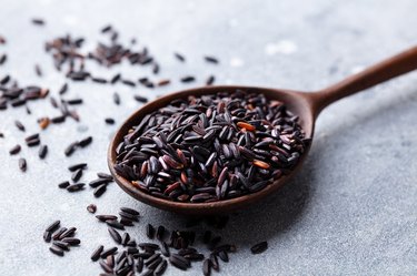 Tyrosine-rich black wild rice in a wooden spoon on a grey stone background