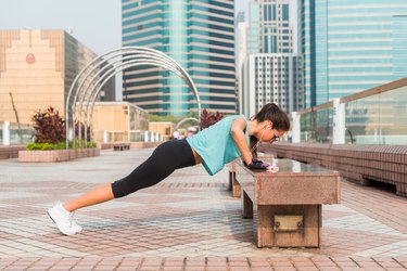 Fitness woman doing feet elevated push-ups on a bench in the city. Sporty girl exercising outdoors