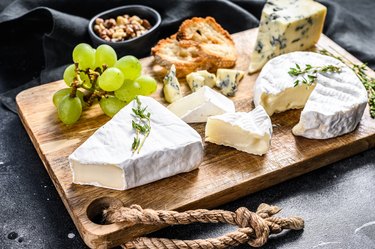 Cheese plate with Camembert, brie and blue cheese with grapes and walnuts. Black background. Top view