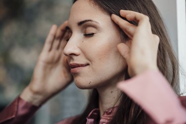 Close up of a person with long brown hair massaging one of the EFT tapping points on their head to relax themselves.