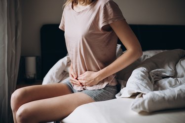 Young person sitting in bed and holding stomach, to illustrate having gas in the morning