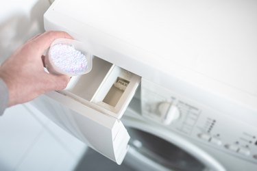 person using dosing aid to pout laundry detergent powder into washing machine