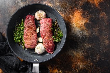 Cooking london broil steak  on grill frying pan with garlic and herbs just from fire top view with smoke space for texture