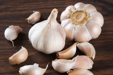 a close up of garlic cloves and two full bulbs on a wooden table