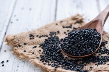 a close up of a wooden spoon of black lentils on a piece of cloth on a wooden table