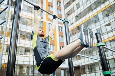 Man doing hanging L-sit, strengthening body on workout ground