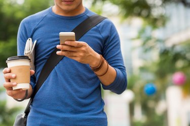 person walking while reading a text message and drinking coffee