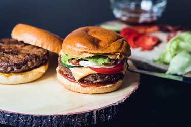 Homemade cheeseburgers with ground beef and venison and ingredients in the background