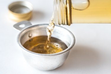 Close up of white vinegar pouring into measuring cup on white background