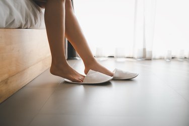 Woman whose feet hurt when she wakes up getting out of bed and putting on slippers