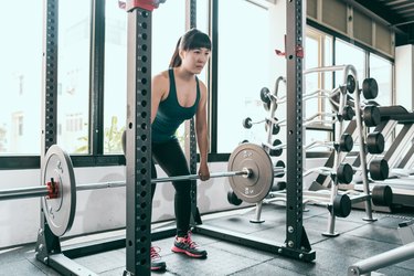 asian woman doing a barbell deadlift on a smith machine at the gym