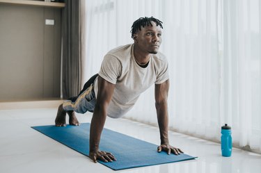 Athlete doing scapular push-ups in living room on blue yoga mat.