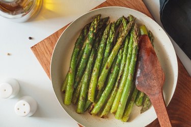 Top view of a plate of roasted asparagus on a wooden board