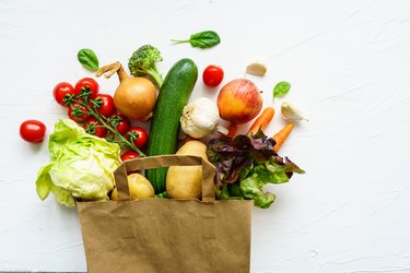 Fresh raw vegetables in a paper shopping bag on a white background