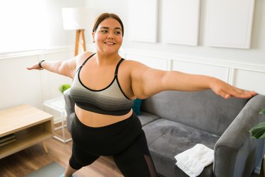 woman smiling while doing yoga in her living room, as a way to practice body acceptance