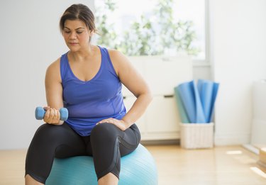 Woman doing biceps curls on a stability ball during a weight-lifting workout
