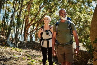 an older couple hiking in the woods, as a way to manage stress with aging