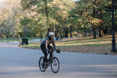 Person riding a bike through a park outside cycling with Achilles tendonitis.
