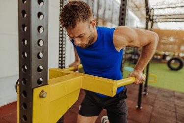 man wearing a blue workout tank and doing a triceps dip at the gym