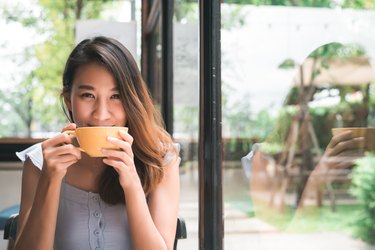 年轻女子喝温暖anti-bloating茶,坐在咖啡馆享受它。