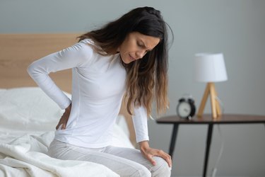 Unhappy woman touching stiff muscles, suffering from backache