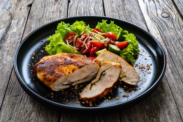 Stuffed chicken breast and vegetables on wooden table