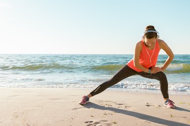 Athletic girl in a red t-shirt stretching on the beach getting fit for summer