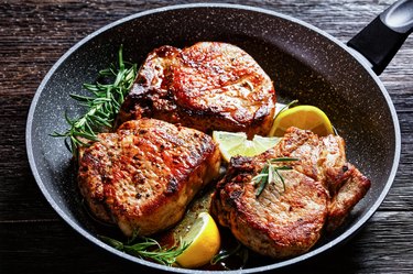 roasted pork karbonade, pork cutlets with rosemary sprigs and lemon slices in a skillet on a wooden table, horizontal view from above